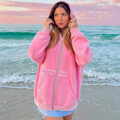 Person wearing a pink hoodie with text on a beach at sunset