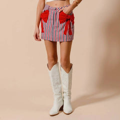 Person wearing a red and white striped skirt with a large bow and white cowboy boots on a beige background