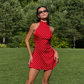 Woman in a red polka dot dress standing on grass with trees in the background
