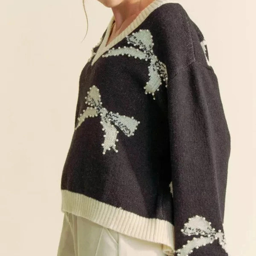 Black sweater with white floral patterns worn by a person on a beige background