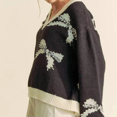Black sweater with white floral patterns worn by a person on a beige background