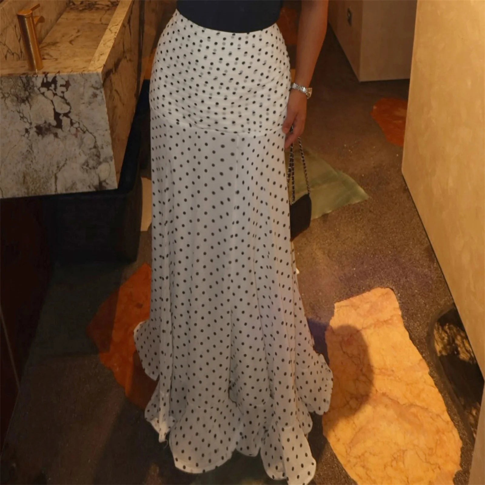 Person wearing a long white polka dot skirt in an indoor setting