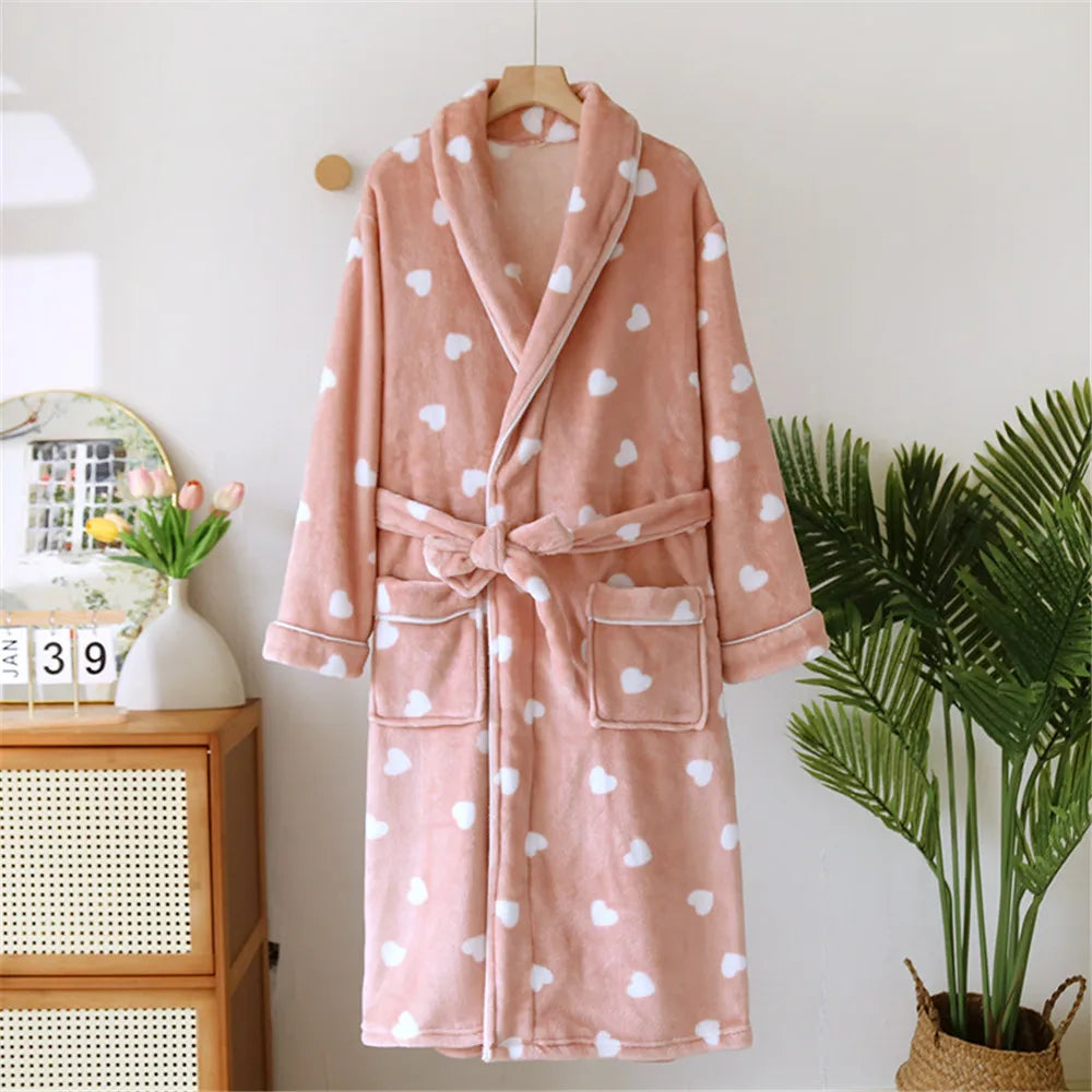 Pink robe with white heart patterns hanging on a wooden hanger against a white wall.