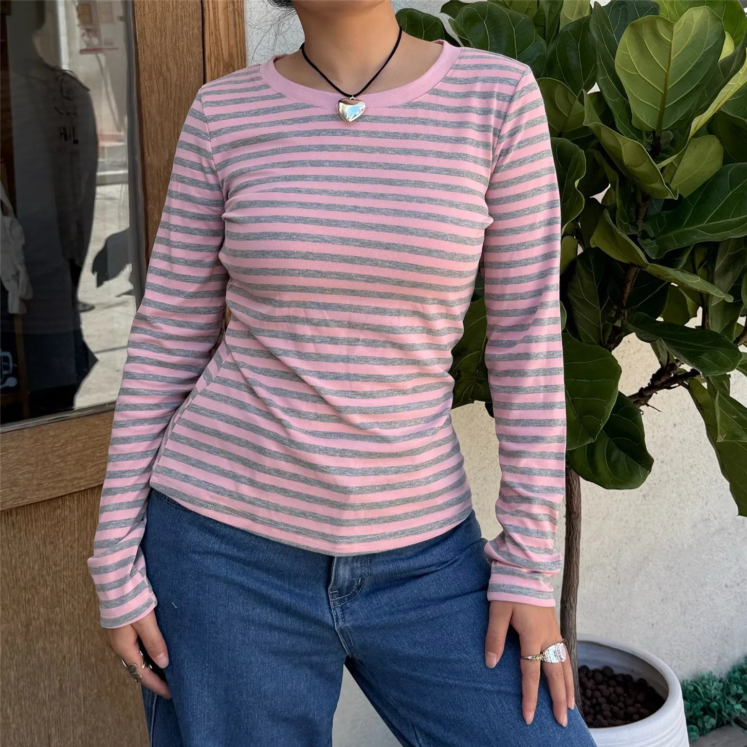 Person wearing a pink and gray striped long-sleeve shirt and blue jeans standing outdoors.