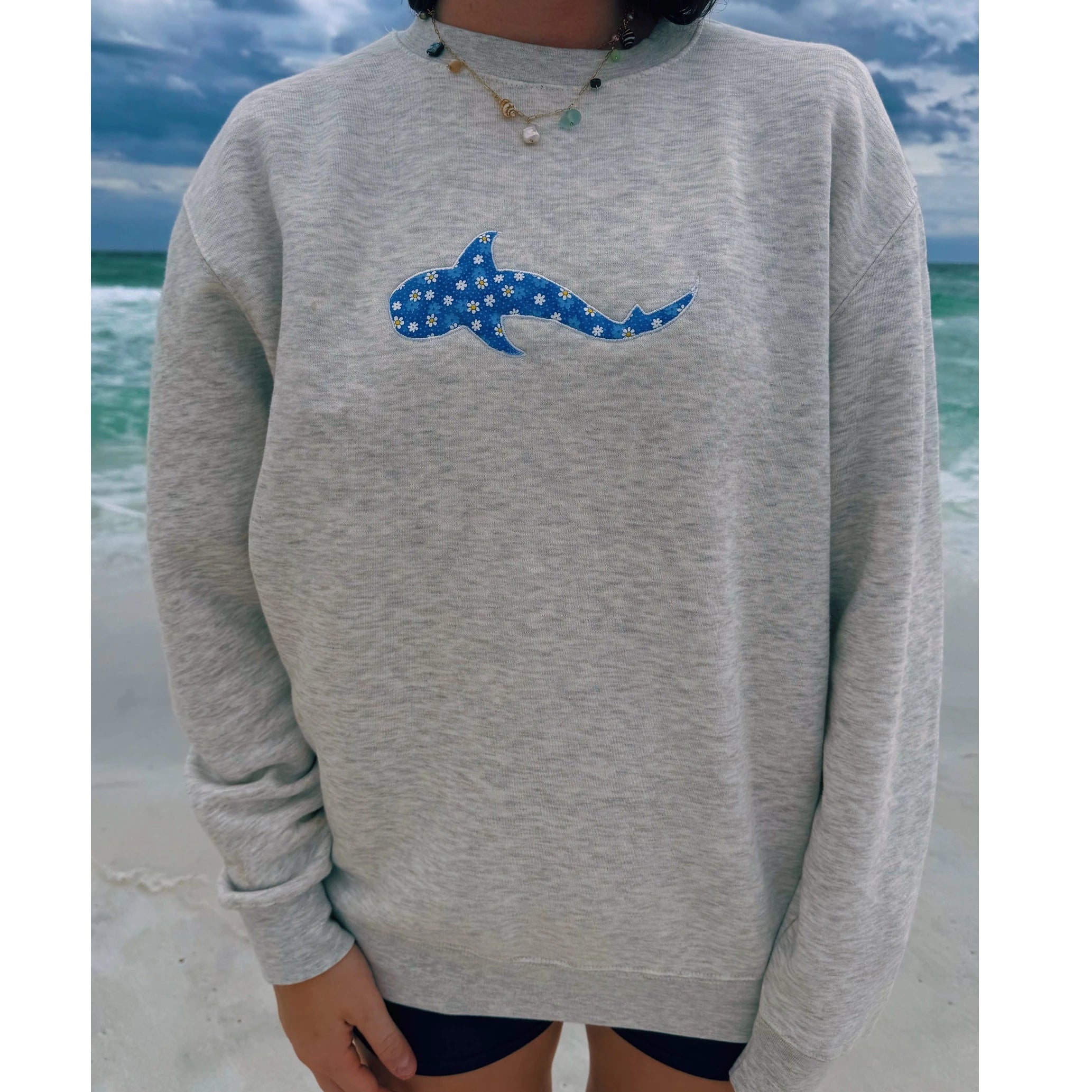 Person wearing a gray sweatshirt with a blue shark design on a beach