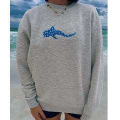Person wearing a gray sweatshirt with a blue shark design on a beach