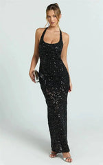 Woman wearing a black sequin halter maxi dress and holding a silver clutch.