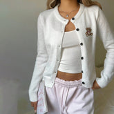 Person wearing a white cardigan with a teddy bear emblem, white top, and pink pants .