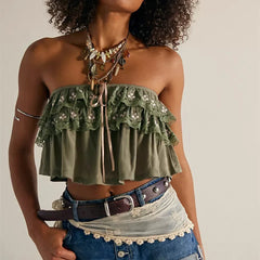 Woman wearing a green strapless top with ruffles and denim shorts against a neutral background