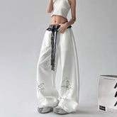 White wide-leg pants with butterfly embroidery and lace details worn by a person on a gray background.