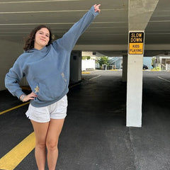 Person in a blue hoodie and white shorts standing in a parking garage with a 'Slow Down Kids Playing' sign.