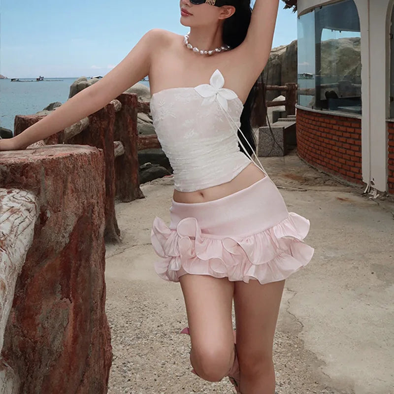Woman in a white top and pink skirt standing by a waterfront with a scenic background.
