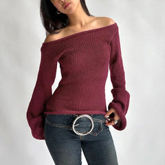 Woman wearing a burgundy off-shoulder sweater and blue jeans with a belt.