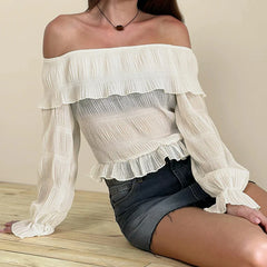 Woman wearing an off-shoulder ruffled top and denim shorts on a wooden floor.