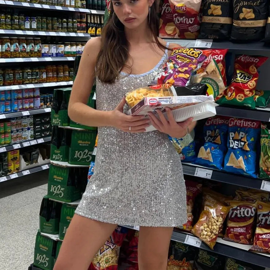 Woman in a silver dress holding snacks in a grocery store aisle