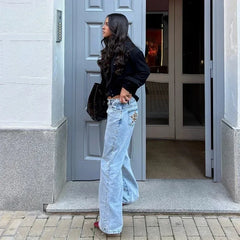 Woman in light blue jeans and black jacket standing in front of a gray door.