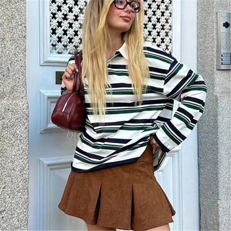 Woman wearing a striped sweater and brown skirt standing in front of a door.