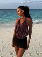 Woman in a burgundy top and black skirt standing on a beach with ocean in the background
