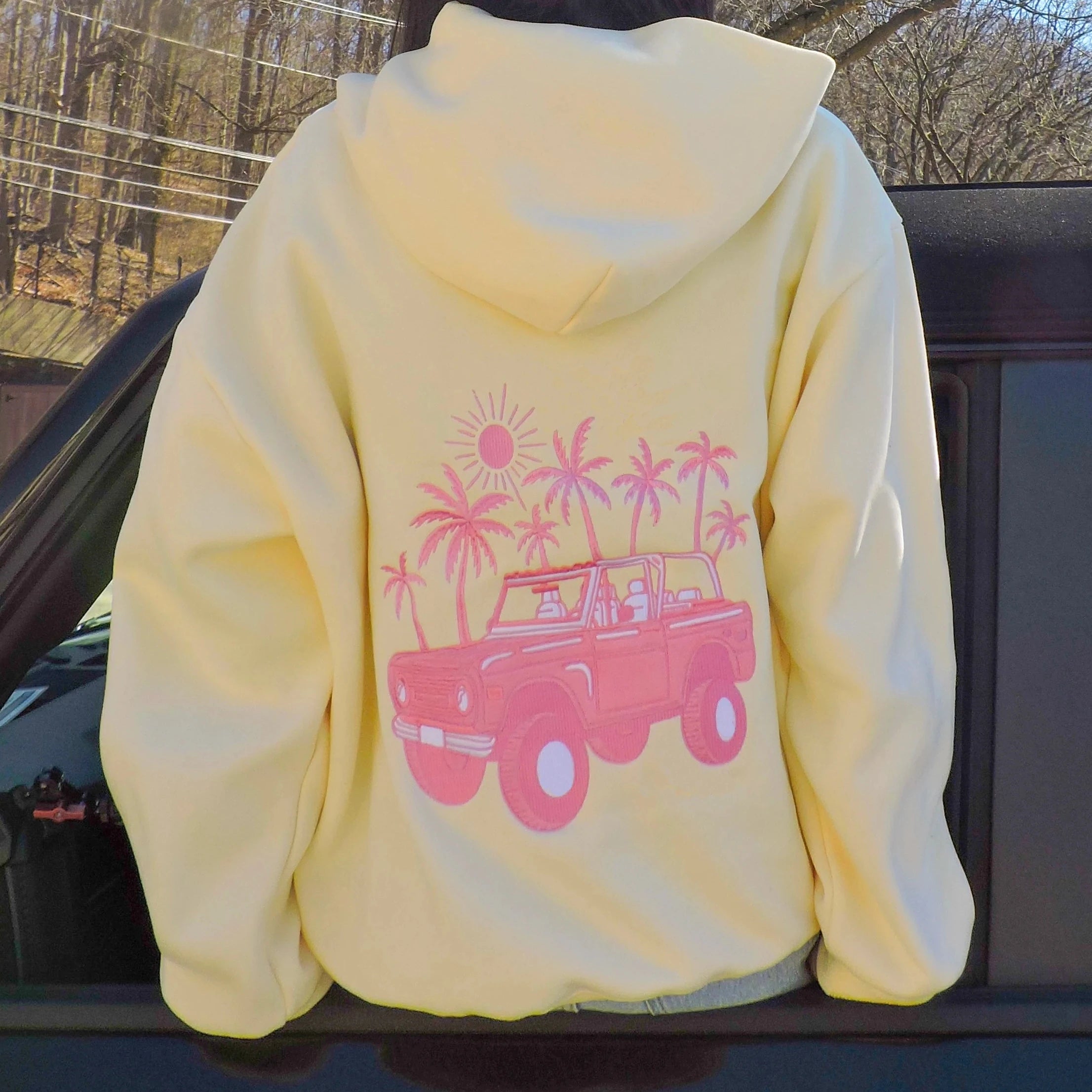 Yellow hoodie with pink graphic of a car and palm trees on a car seat.