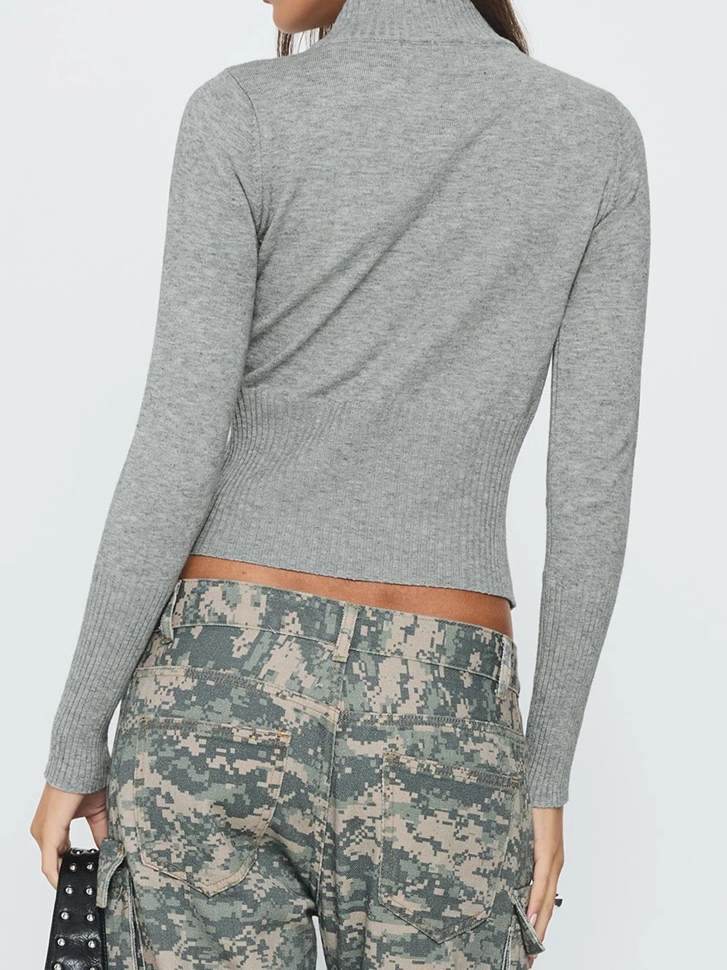 Person wearing a gray ribbed sweater and camouflage pants on a white background