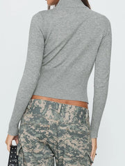 Person wearing a gray ribbed sweater and camouflage pants on a white background