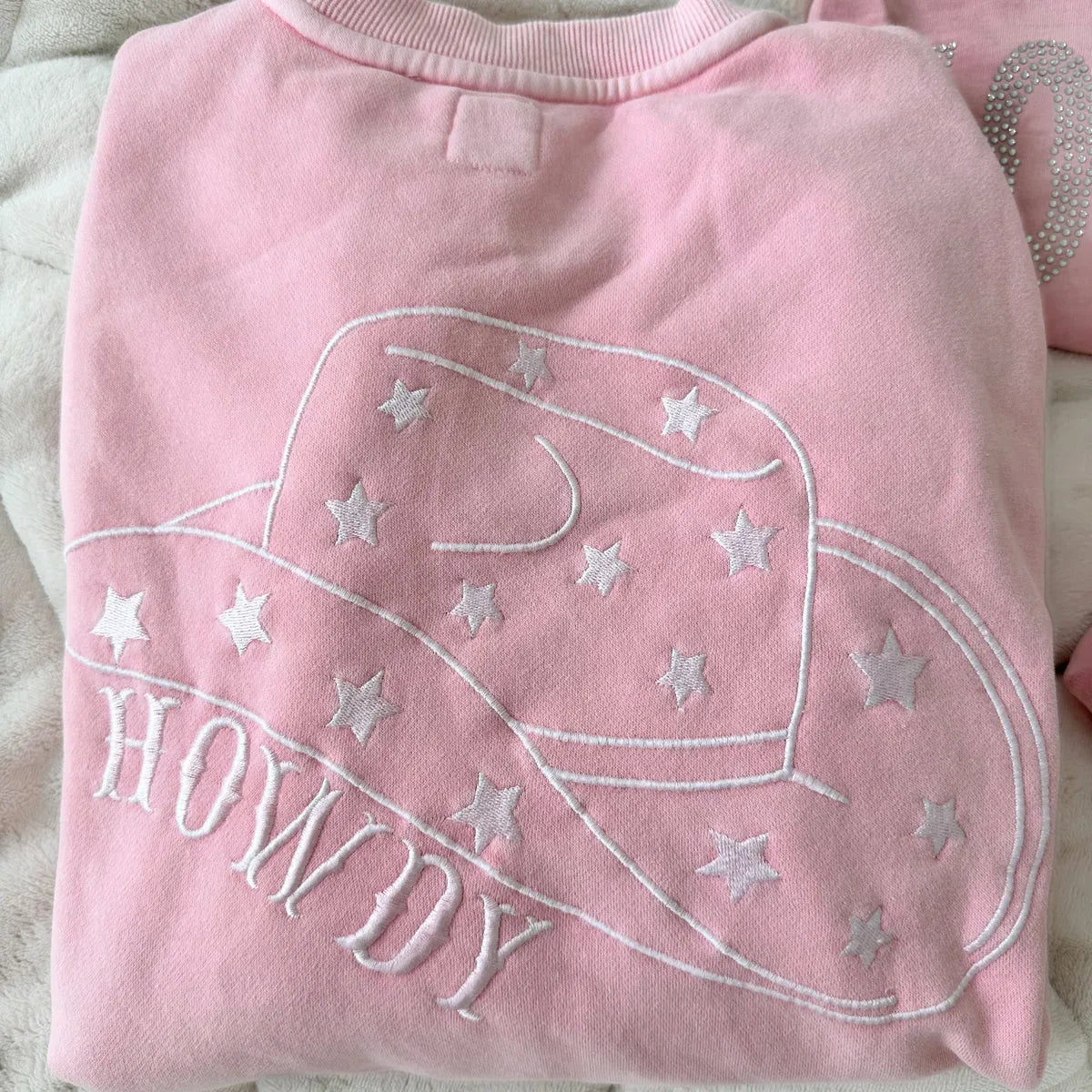 Pink sweatshirt with 'HOWDY' and cowboy hat design on a light background