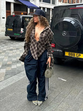 Woman in plaid shirt and dark pants standing on a street with vehicles in the background