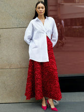 Woman wearing a white shirt and red skirt standing against a building.