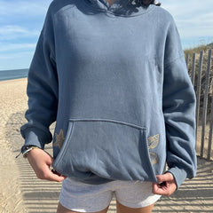 Person wearing a blue hoodie with leaf designs on a beach