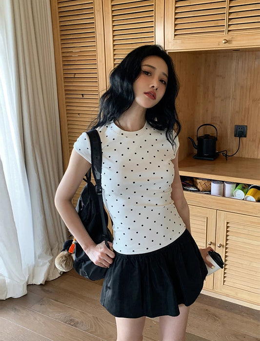 Woman in a polka dot shirt and black skirt standing in a room with wooden cabinets.