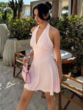 Woman in a light pink dress standing outdoors with greenery and furniture in the background