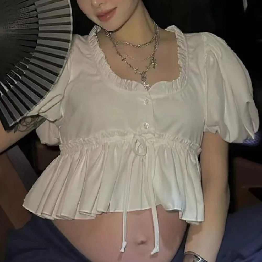 Person wearing a white blouse with ruffled details, sitting indoors.