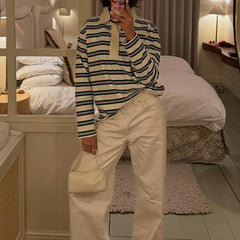 Person taking a mirror selfie wearing a striped shirt and beige pants in a bedroom.