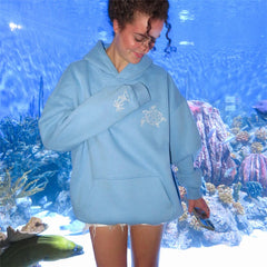 Person wearing a light blue hoodie with turtle designs in front of an aquarium.