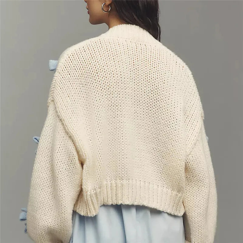 Person wearing a beige knitted cardigan against a gray background