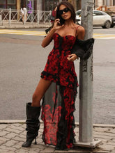 Woman in a red and black floral dress with black boots standing on a street.