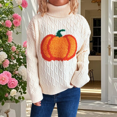 Person wearing a cream sweater with a pumpkin design in front of a floral arrangement.