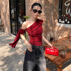 Woman in a red top and sunglasses standing outdoors near a brick wall.