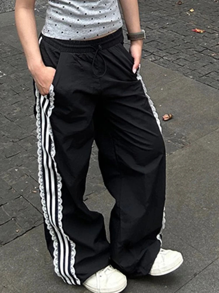 Person wearing black track pants with white stripes on a paved surface