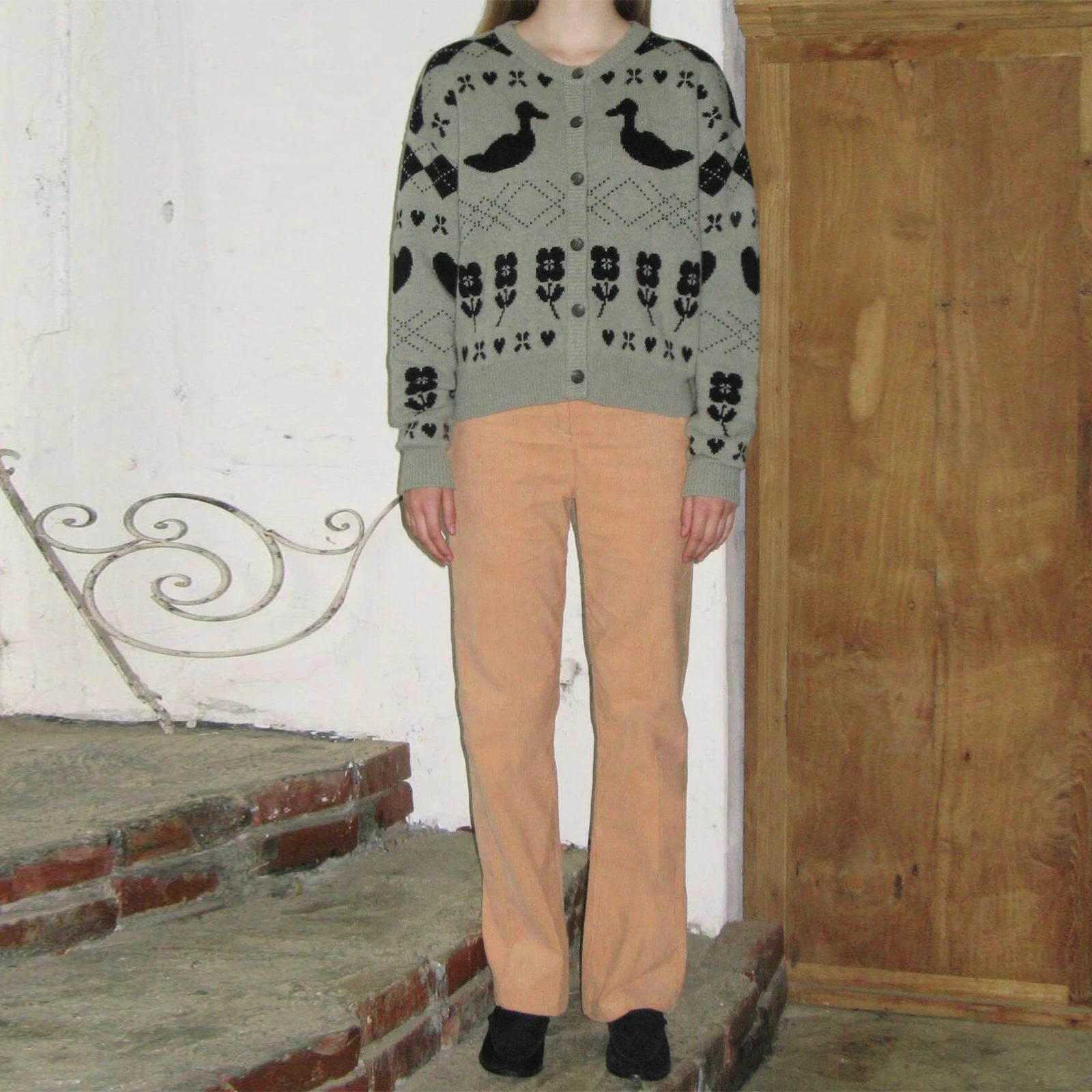 Person wearing a patterned sweater and beige pants standing on stone steps.