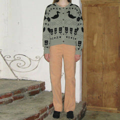 Person wearing a patterned sweater and beige pants standing on stone steps.