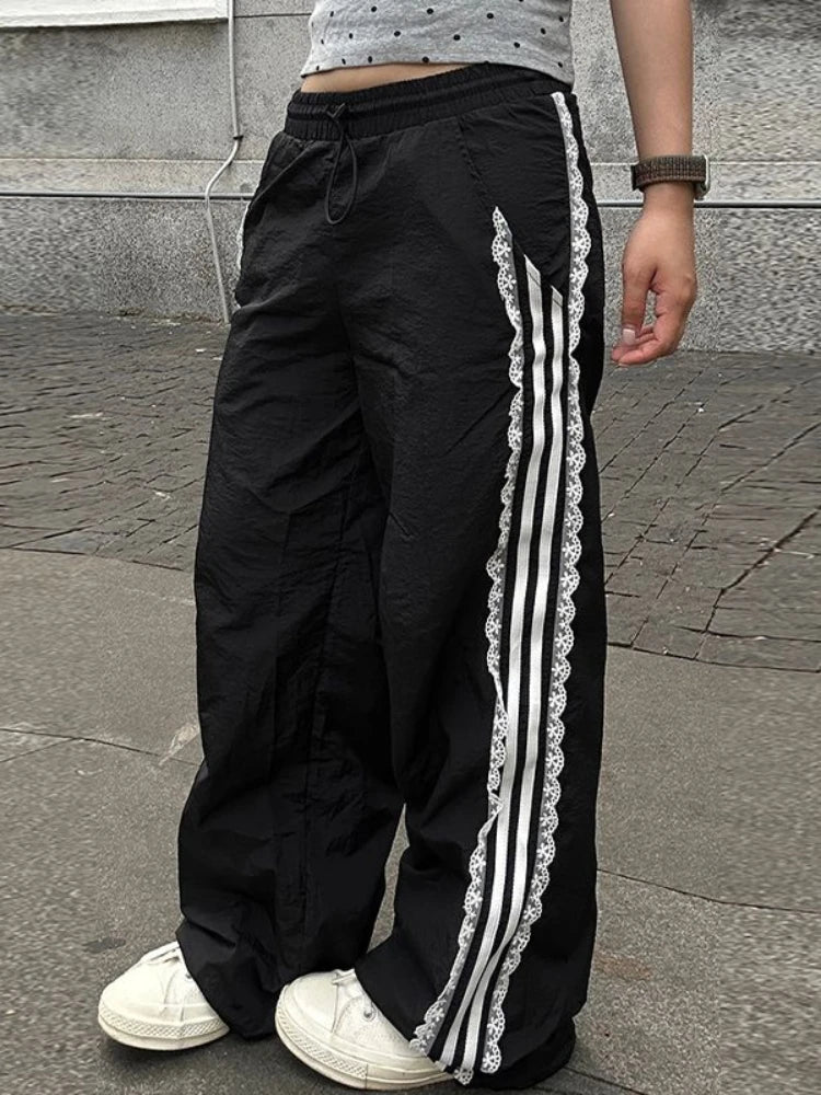 Black track pants with white stripes and lace trim worn by a person on a pavement.
