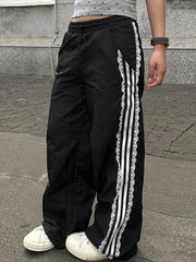Black track pants with white stripes and lace trim worn by a person on a pavement.