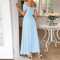 Woman in a light blue off-shoulder dress standing in a bright room with a table and flowers.