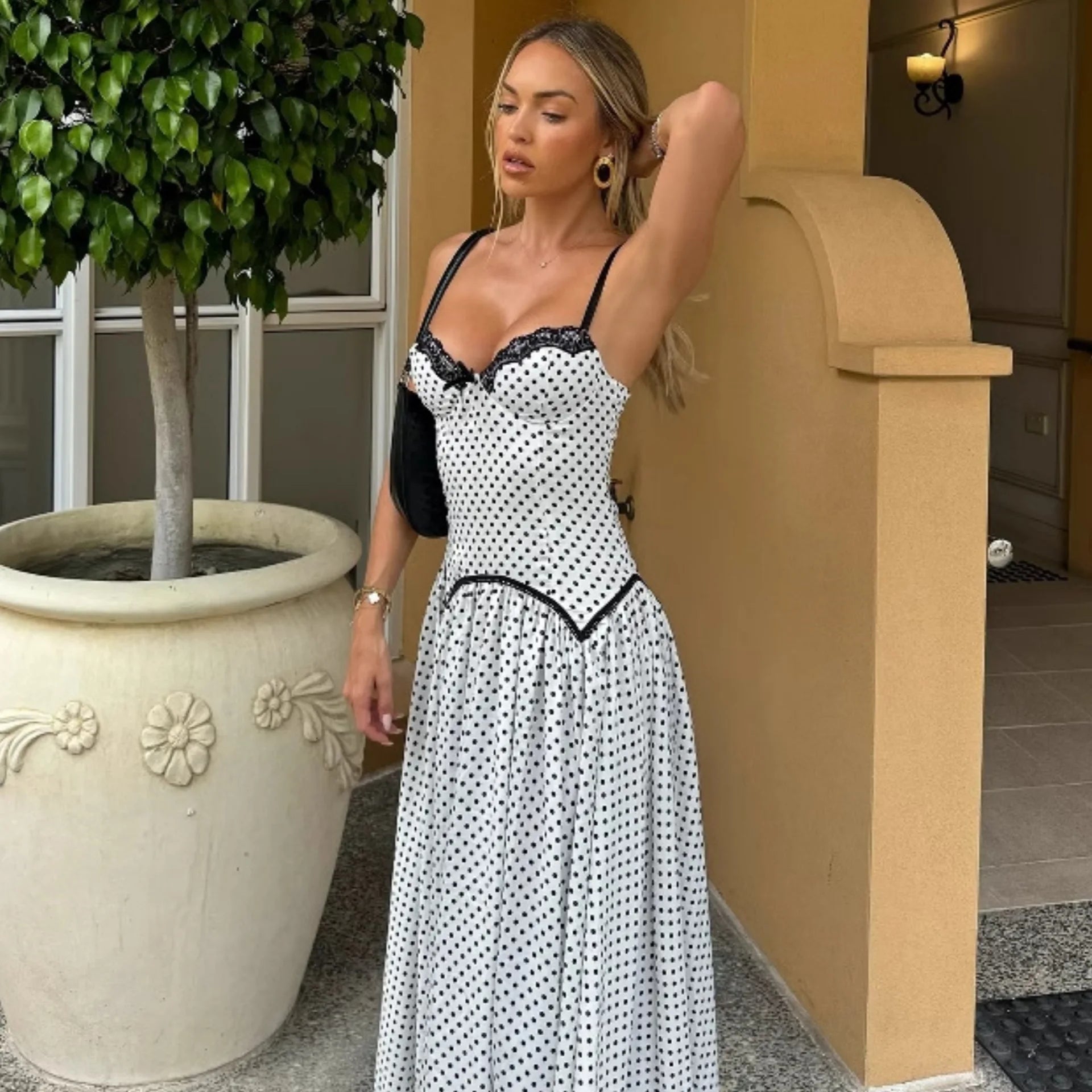 Woman in a polka dot dress standing outdoors next to a potted plant.