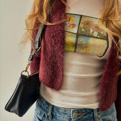 Person wearing a maroon scarf, white shirt with autumn design, and blue jeans, holding a black handbag.