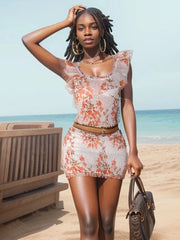 Woman in a floral dress standing on a beach with a clear blue sky.