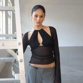 Woman wearing a black long-sleeve top with cut-out design and gray pants in an indoor setting.