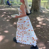Woman in a white dress with red floral patterns walking in a park.