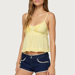 Woman wearing a yellow lace top and blue denim shorts on a white background
